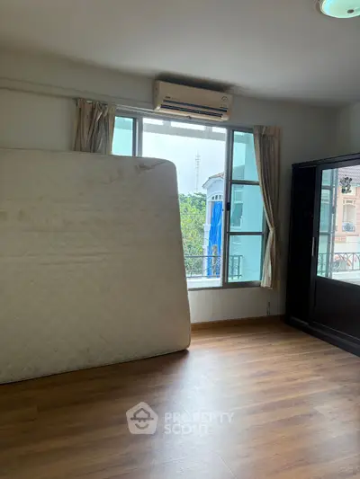 Spacious bedroom with large window and wooden flooring, featuring an air conditioner and wardrobe.