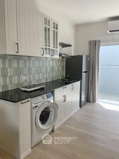 Modern kitchen with sleek cabinetry, washing machine, and fridge in bright natural light.