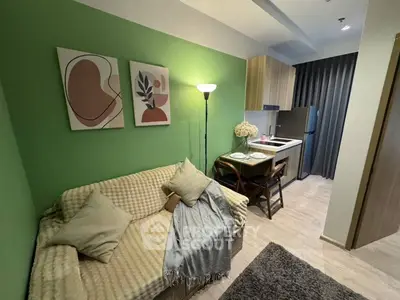 Cozy modern living room with green accent wall, stylish decor, and compact kitchen area.