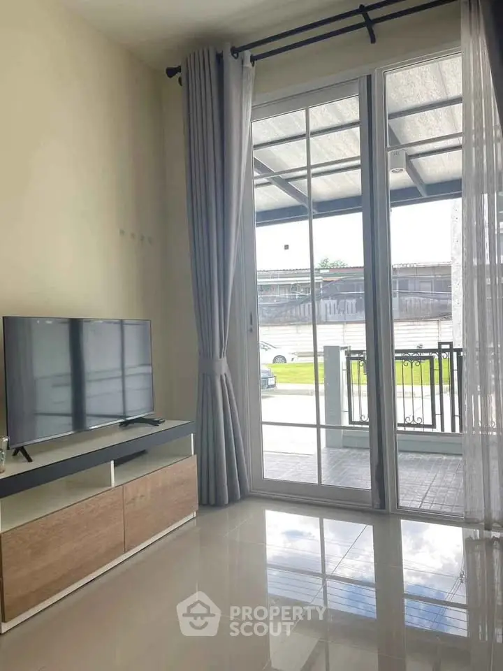 Modern living room with large glass doors leading to a patio, featuring sleek TV stand and elegant curtains.