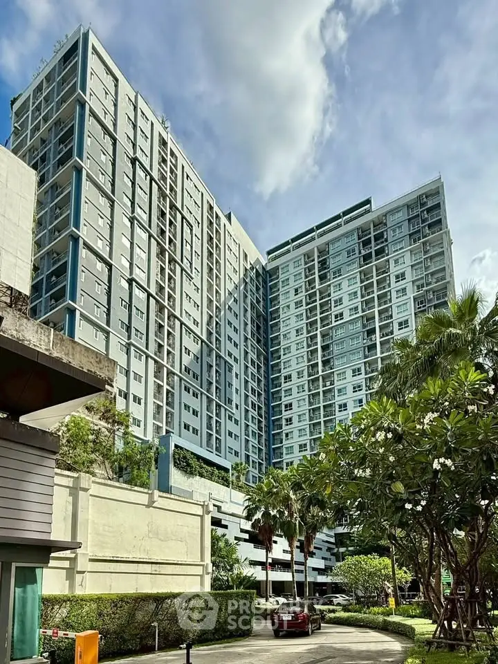 Modern high-rise residential building with lush greenery and clear skies.