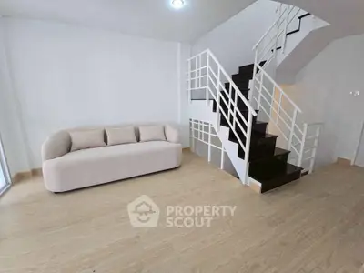 Modern living room with stylish staircase and cozy sofa, featuring sleek wooden flooring.