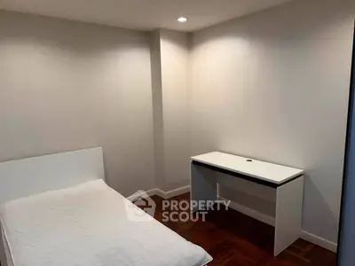 Minimalist bedroom with single bed and desk, featuring wooden flooring and recessed lighting.