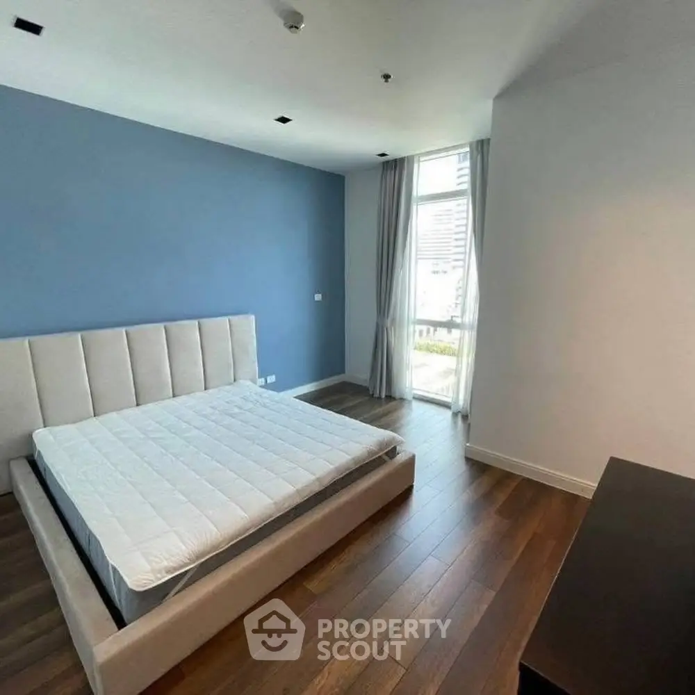 Modern bedroom with blue accent wall and large window in a stylish apartment.