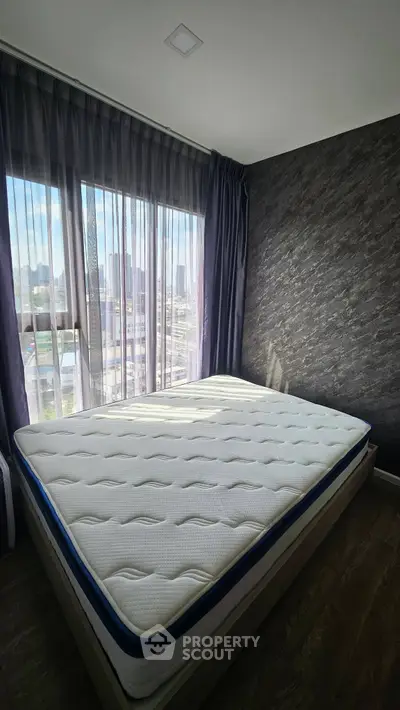 Modern bedroom with large window and city view, featuring a comfortable mattress and stylish decor.