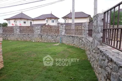 Charming stone-walled garden with lush green lawn and view of elegant houses in the background.