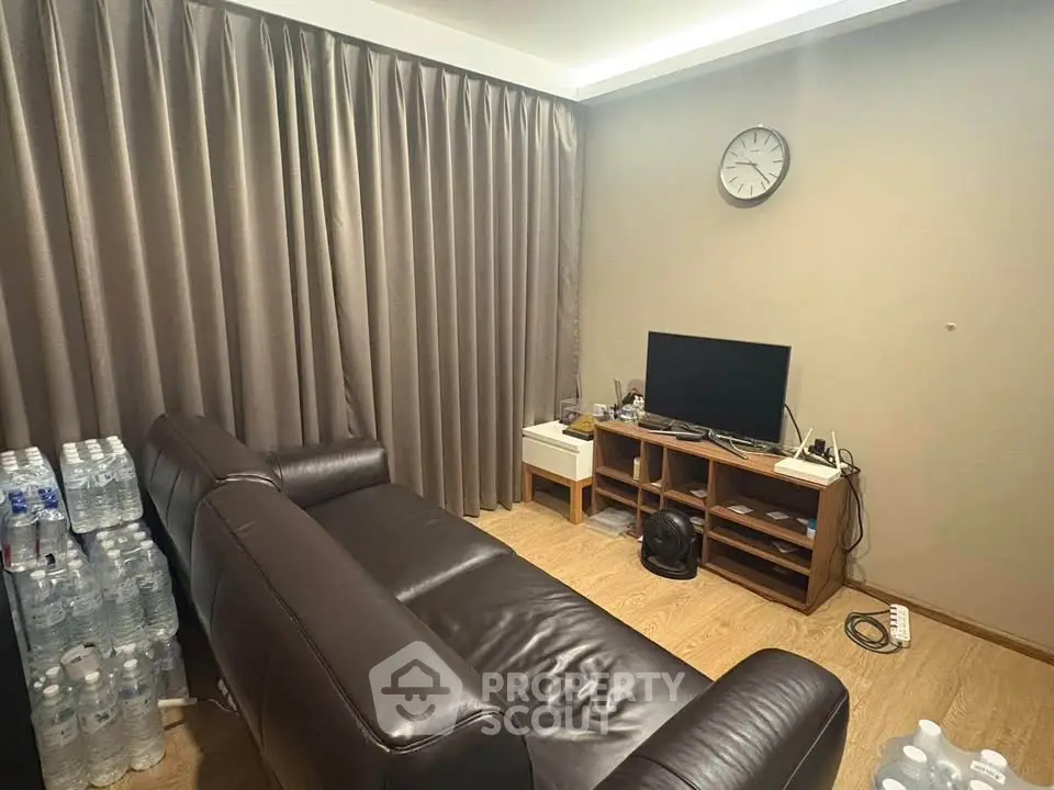Cozy living room with leather sofa and TV, featuring elegant curtains and wooden flooring.