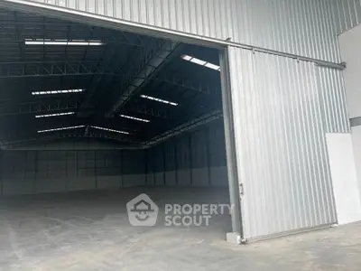 Spacious industrial warehouse with high ceilings and large sliding door, ideal for storage or manufacturing.