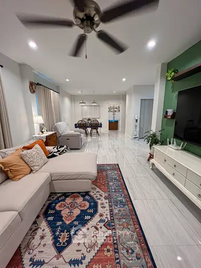 Spacious living room with modern decor and ceiling fan, featuring a cozy sectional sofa and vibrant area rug.