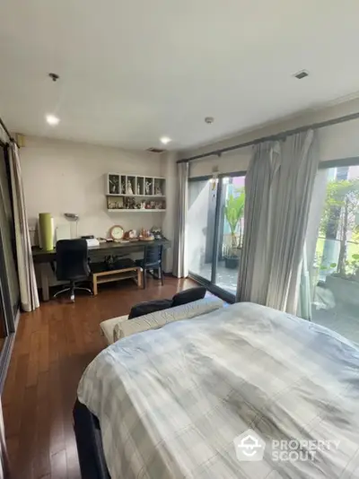 Spacious bedroom with garden view and study area, featuring large windows and wooden flooring.