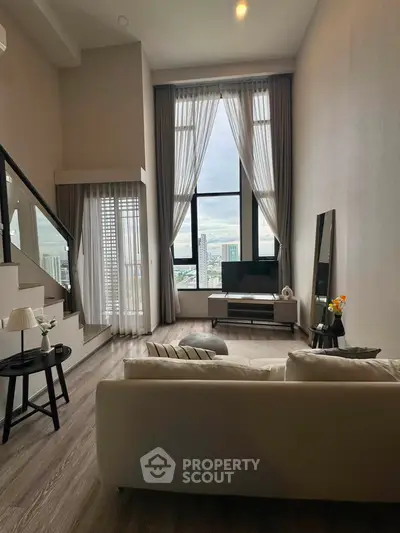 Spacious modern living room with high ceilings and city view, featuring elegant decor and natural light.