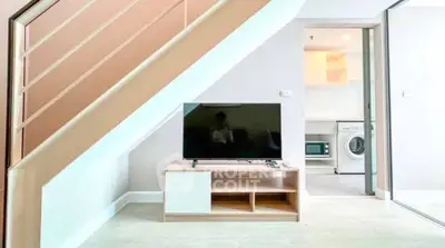 Modern living space with TV under staircase and view into laundry area with washing machine.