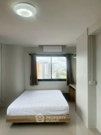 Modern bedroom with city view, featuring a cozy bed and large window for natural light.
