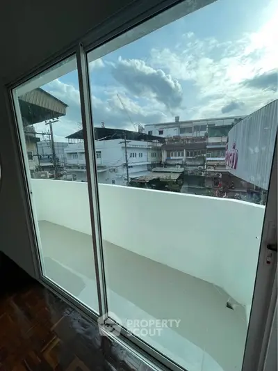 Spacious balcony with sliding glass doors offering a cityscape view, perfect for relaxation.