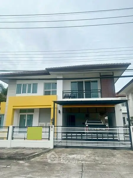 Modern two-story house with yellow accents and covered parking in a suburban neighborhood.