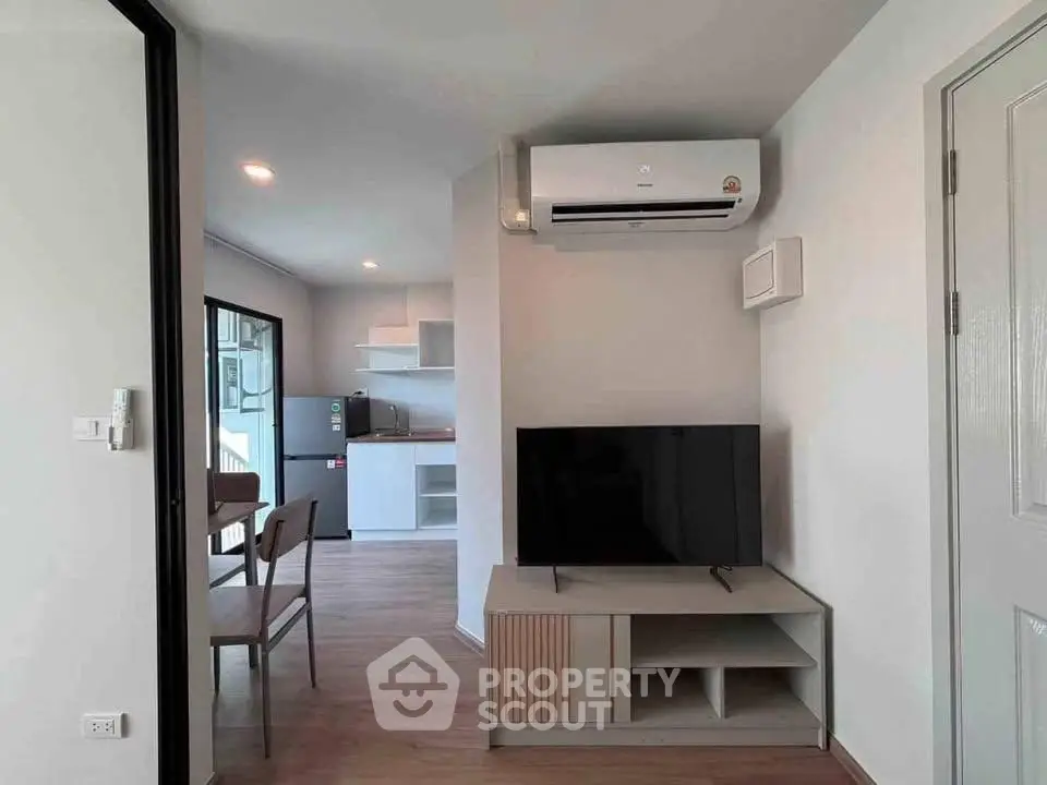 Modern living room with sleek TV setup and open kitchen layout in stylish apartment.