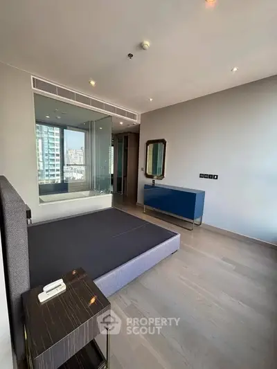 Modern bedroom with large window and sleek furnishings in urban apartment.