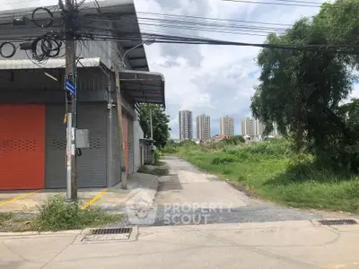 Industrial warehouse with orange shutters near urban high-rise buildings and greenery.