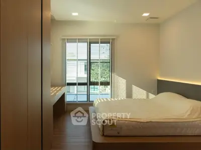 Modern bedroom with large window and natural light, featuring a minimalist design and wooden flooring.
