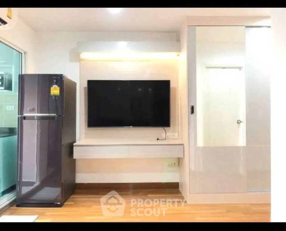 Modern living room with sleek TV setup and stylish refrigerator in a bright apartment.