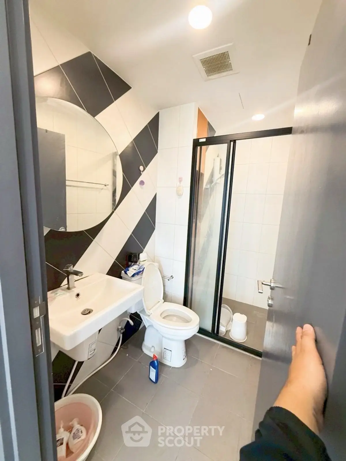 Modern bathroom with sleek design, featuring a round mirror, glass shower, and contemporary fixtures.