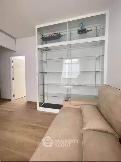 Modern living room with beige sofa and glass display cabinet, featuring sleek wooden flooring.