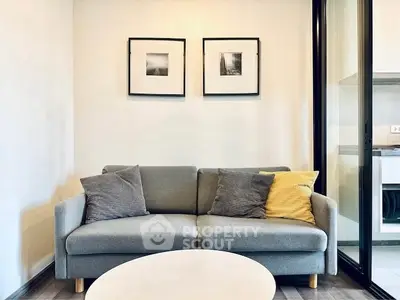 Modern living room with stylish sofa and framed art, adjacent to sleek kitchen area.