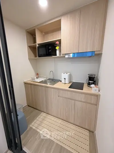 Modern compact kitchen with wooden cabinets and sleek appliances in a cozy apartment.