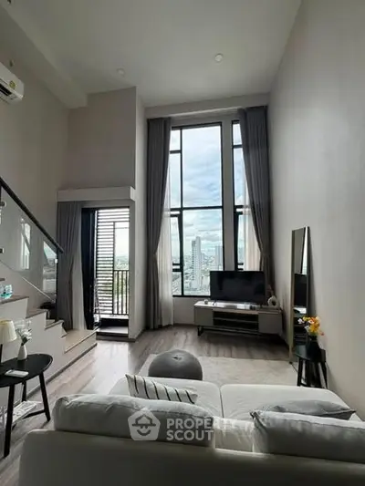 Modern loft-style living room with high ceilings and city view, featuring sleek furniture and large windows.