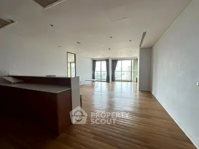 Spacious modern living room with wooden flooring and large windows offering city views.