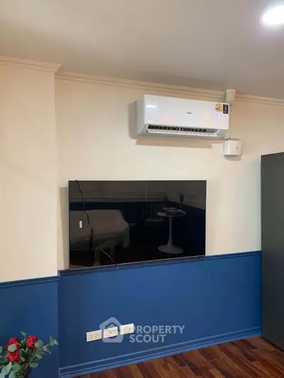 Modern living room with mounted TV and air conditioning unit, featuring stylish blue accent wall.