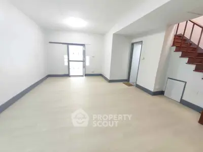 Spacious empty room with light wood flooring and staircase, ideal for customization.