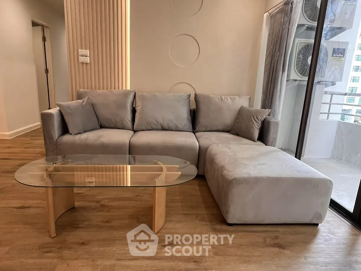 Modern living room with stylish gray sectional sofa and glass coffee table on wooden floor.
