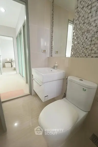 Modern bathroom with sleek fixtures and neutral tiles, leading to a bright bedroom.