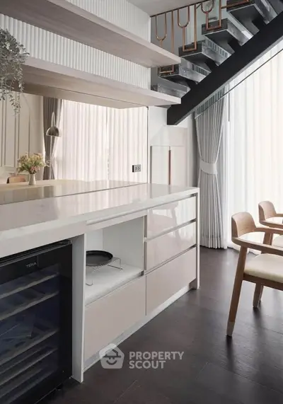 Modern kitchen with sleek design, featuring open layout and stylish dining area under staircase.