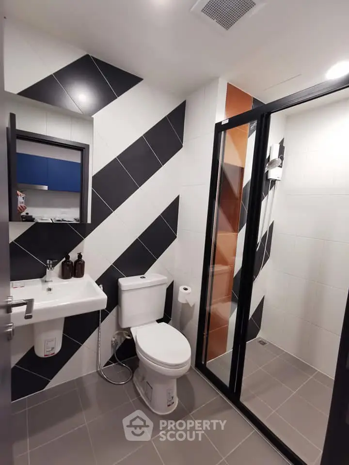 Modern bathroom with sleek black and white diagonal tiles and glass shower enclosure.