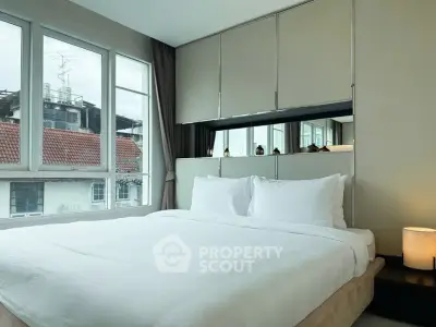 Cozy bedroom with large windows and modern decor, offering a serene urban view.