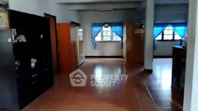 Spacious living area with tiled flooring and large windows with blue curtains.