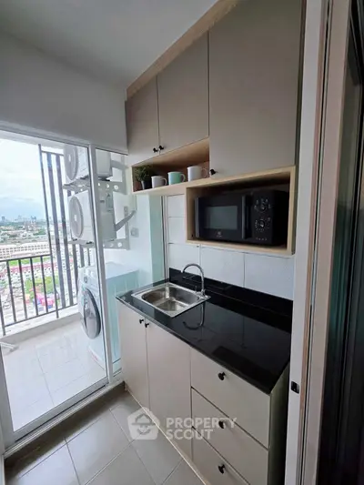 Modern compact kitchen with balcony view, featuring sleek cabinetry, microwave, and washing machine.