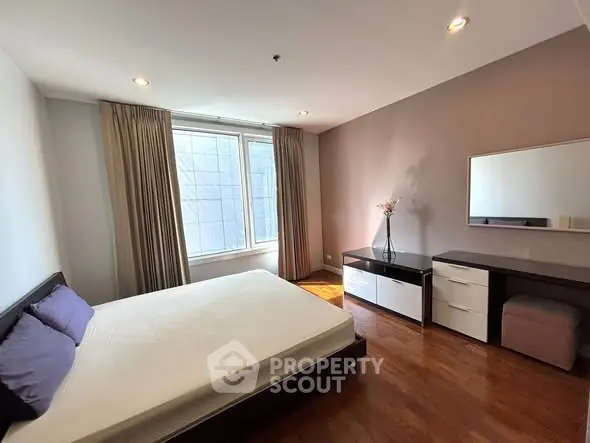 Spacious bedroom with large window and modern furnishings in a stylish apartment.
