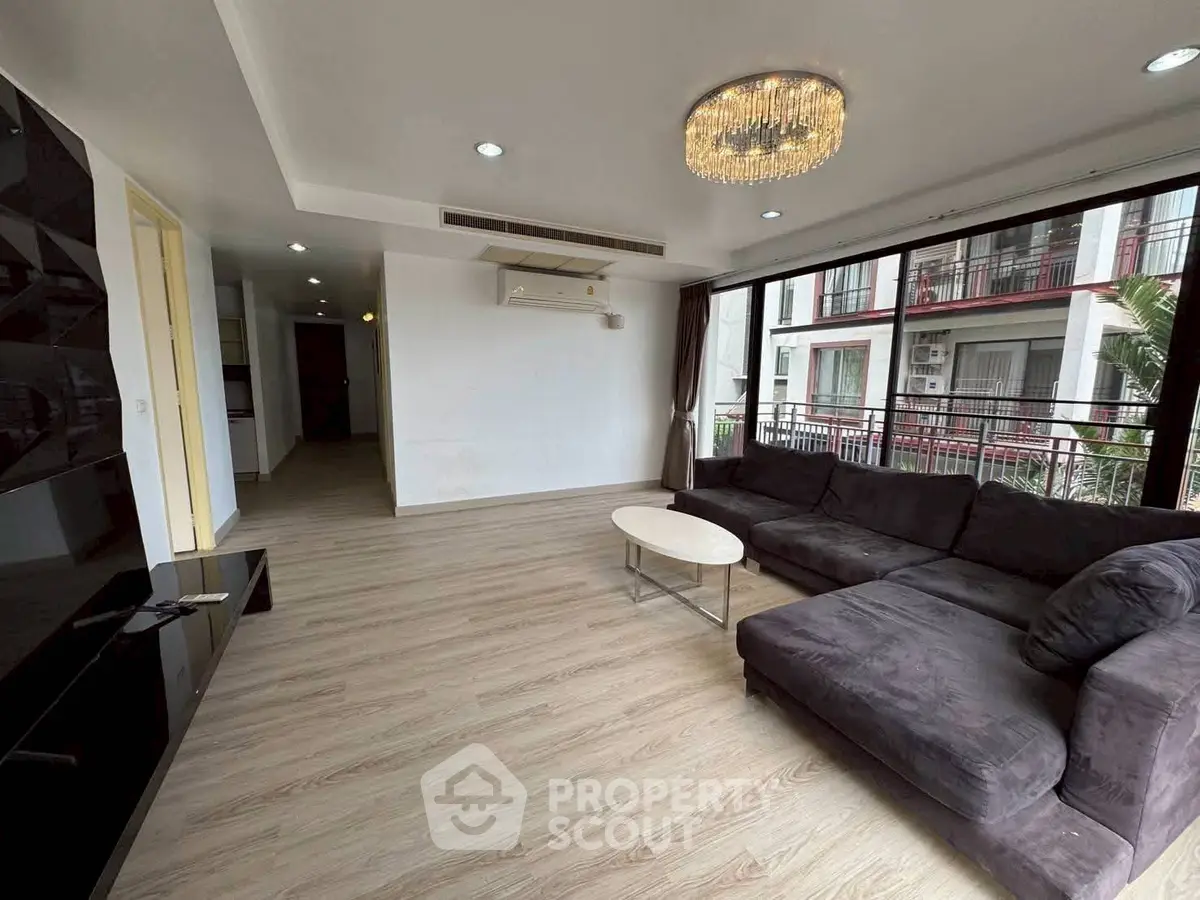 Spacious modern living room with large windows and elegant chandelier in a stylish apartment.