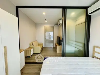 Modern studio apartment with glass partition, cozy living area, and sleek wooden flooring.