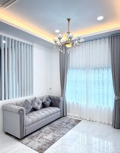 Elegant living room with luxurious chandelier and plush sofa, featuring modern decor and ample natural light.
