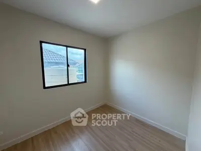 Bright empty room with wooden flooring and large window offering natural light.