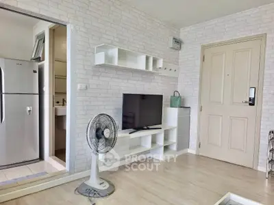 Modern living room with stylish decor and open layout, featuring a TV and fan, adjacent to a compact kitchen.
