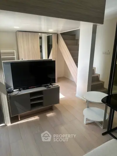 Modern living room with sleek TV setup and stylish staircase in a contemporary apartment.