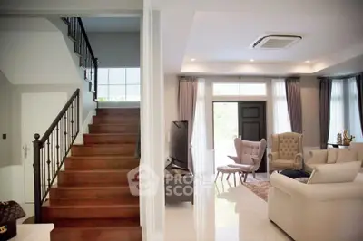 Elegant living room with staircase, featuring modern furniture and natural light.