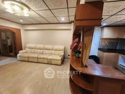 Spacious living room with elegant ceiling design and cozy beige sofa, adjacent to a modern kitchen.