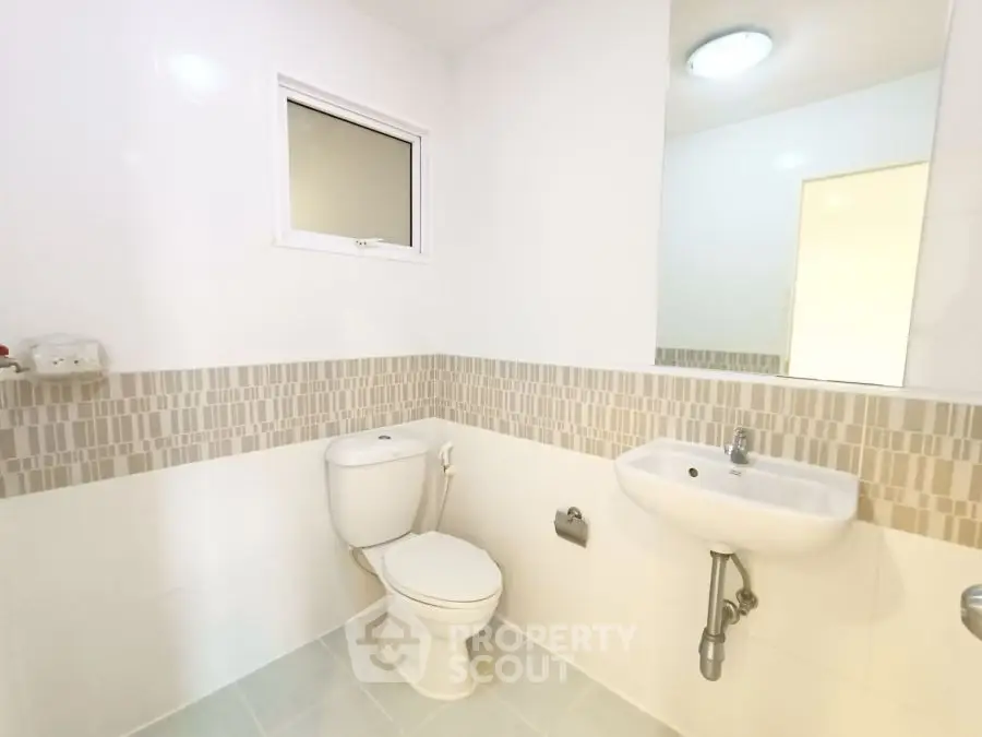 Modern bathroom with sleek design and neutral tiles, featuring a toilet and sink.