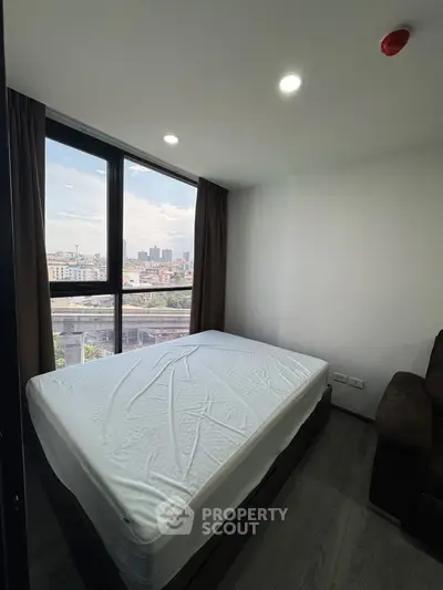 Modern bedroom with large window offering city view, featuring a comfortable bed and sleek design.